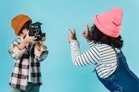 Two children in playful poses indoors capturing moments with a vintage camera.